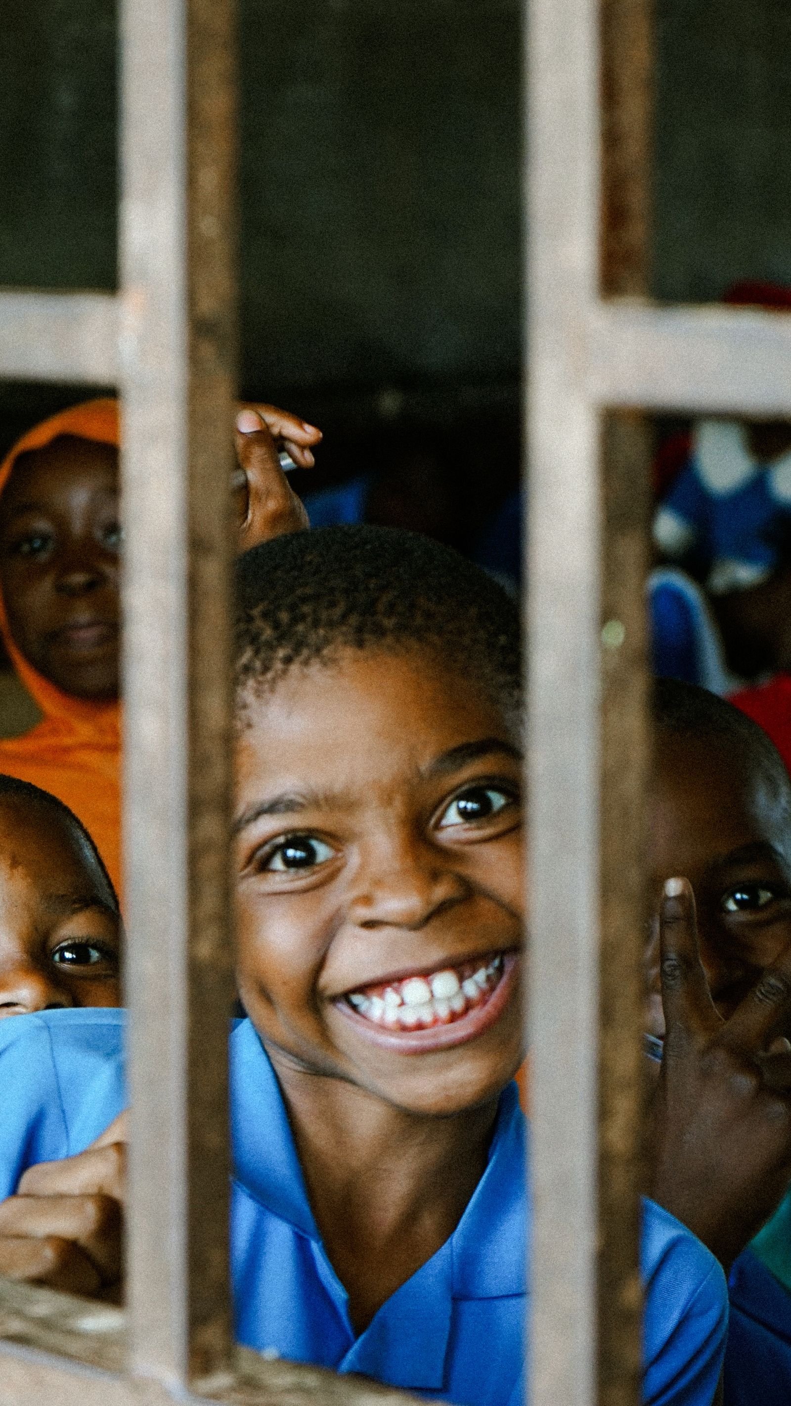 Enfant souriant regardant à travers les barreaux de la fenêtre de sa classe