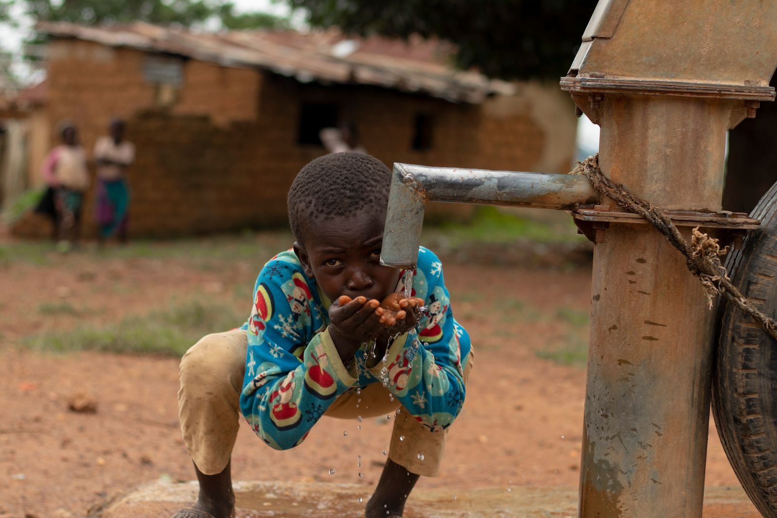 Jeune garçon buvant l'eau d'une pompe manuelle dans un village