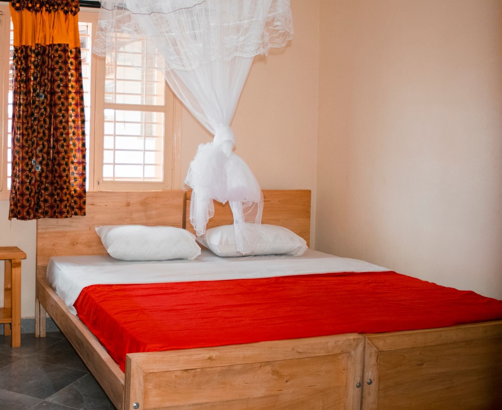 Chambre lumineuse avec lit en bois, couverture rouge et moustiquaire