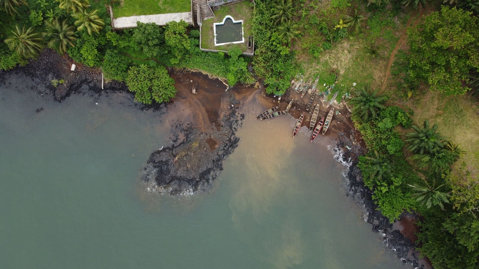 Vue aérienne d'une crique aux roches volcaniques, pirogues tirées sur la rive et forêt tropicale