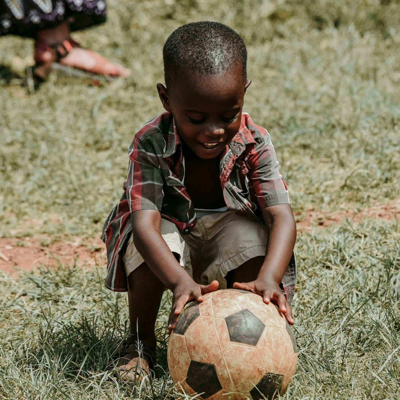 Petit garçon souriant accroupi, les mains posées sur un ballon de football